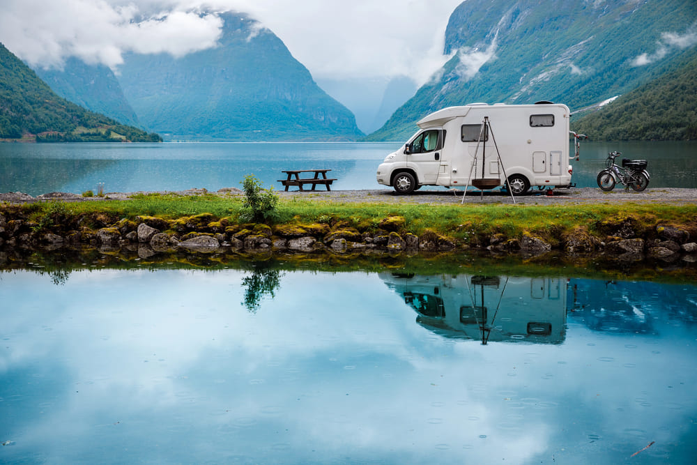 Camper parcheggiato in riva a un lago in autunno, circondato da montagne e paesaggi naturali